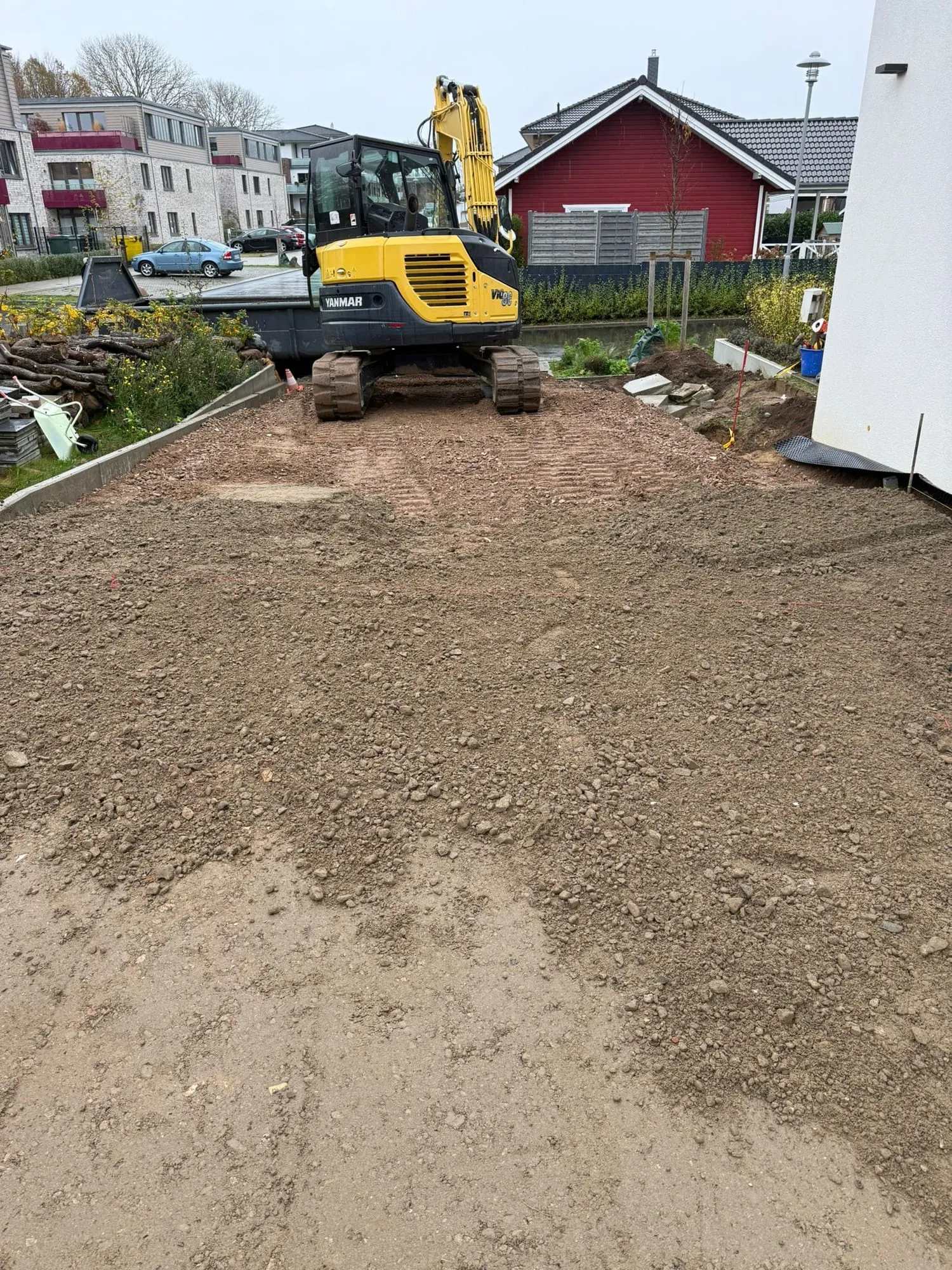 Kettenbagger auf einer modellierten Erdfläche zwischen Wohnhäusern, das Planum ist abgezogen