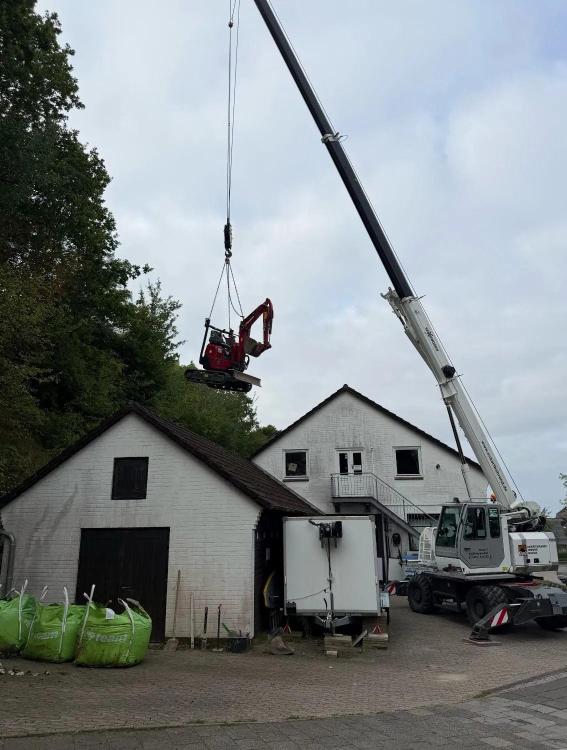 Der Minibagger wird per Kran hinter das Haus gehoben