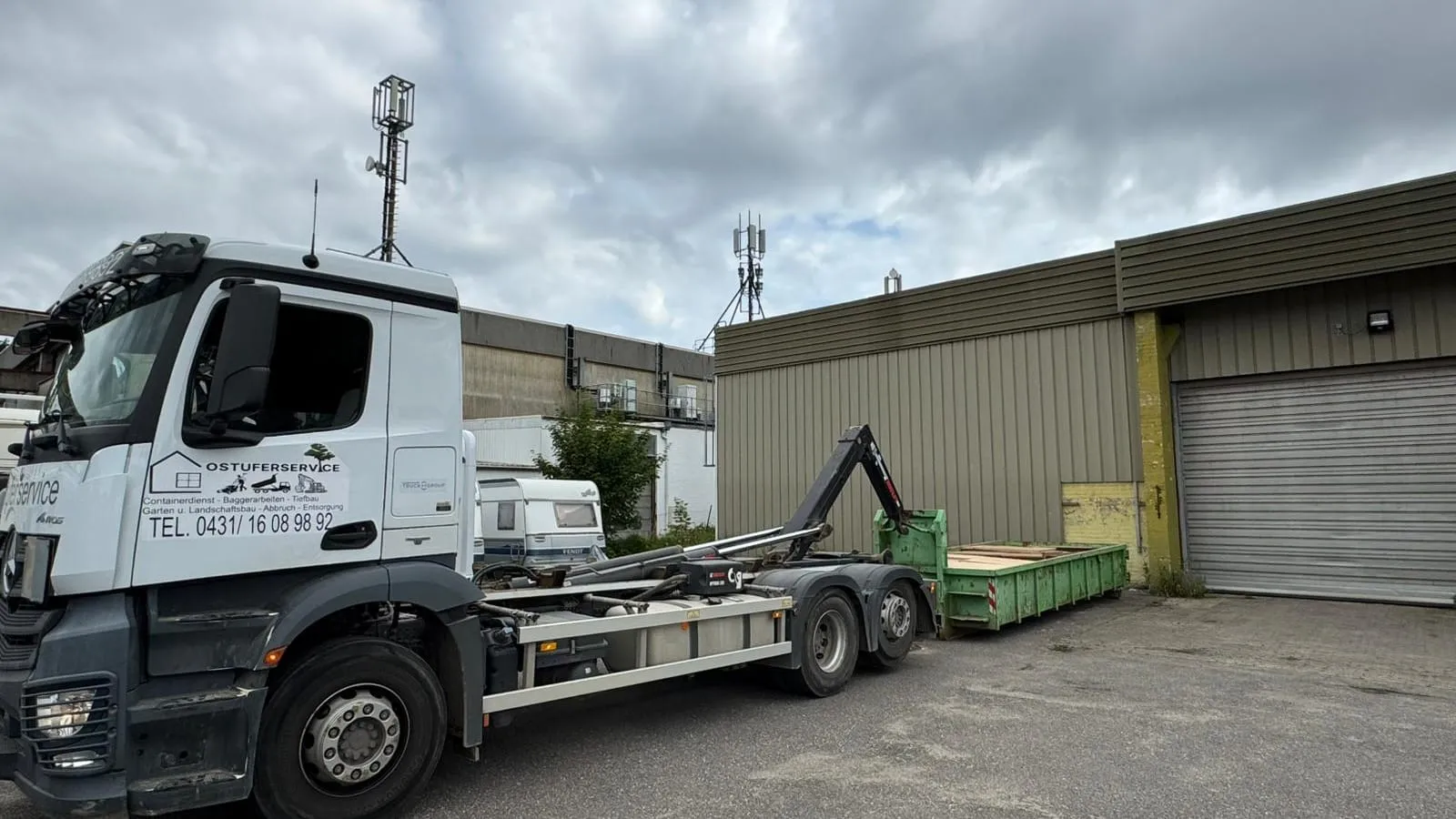 Abrollkipper des Betriebs mit Container vor der Halle auf dem Betriebshof