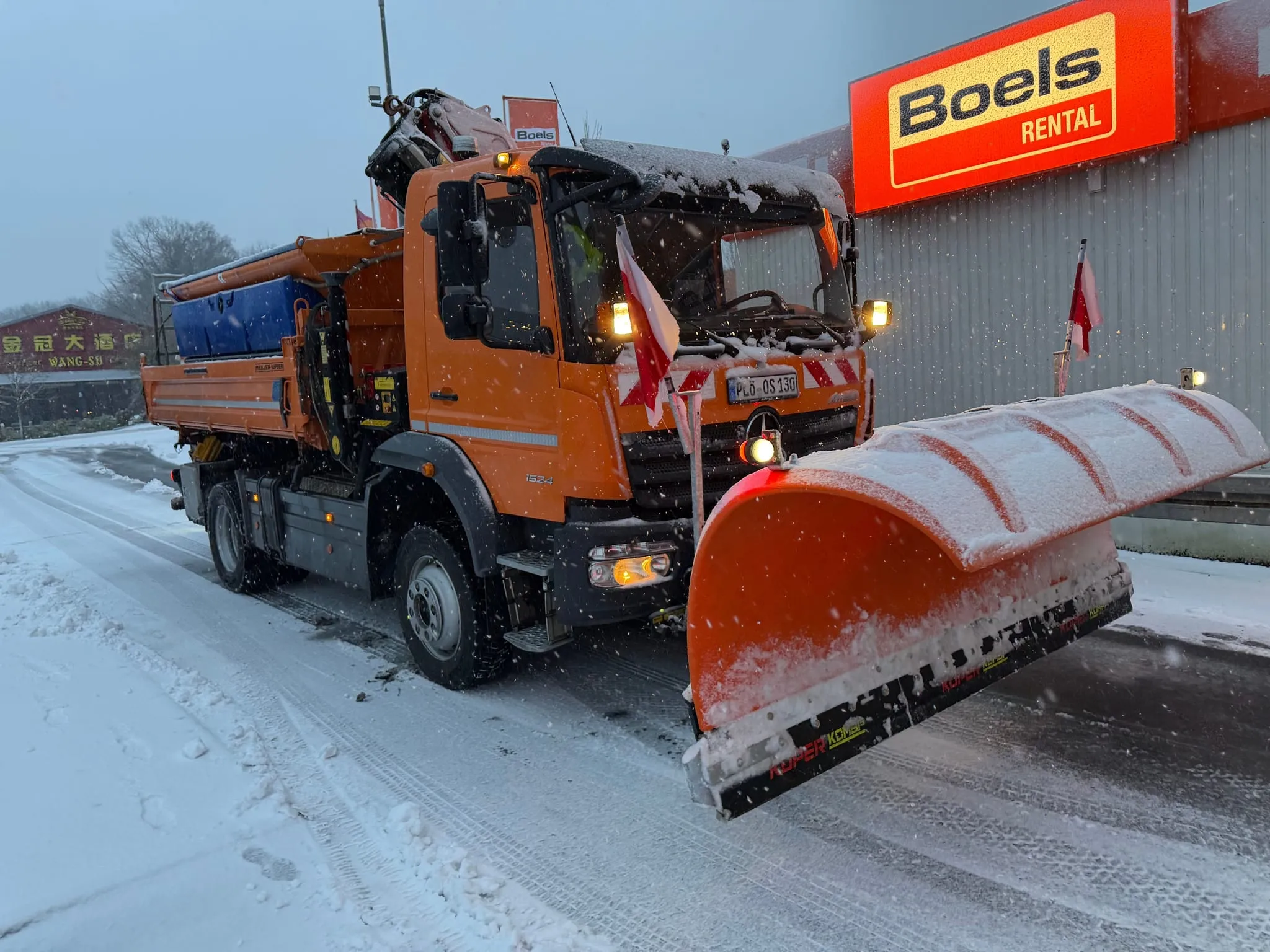Räumfahrzeug mit Schneepflug und Streuer im Einsatz auf einem verschneiten Gewerbegelände.