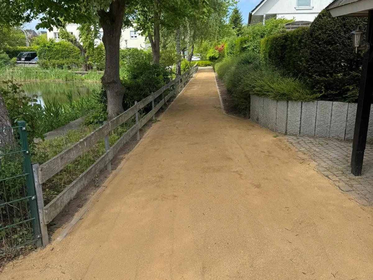 Fertiger wassergebundener Weg zwischen Hecke und Holzgeländer unter alten Bäumen