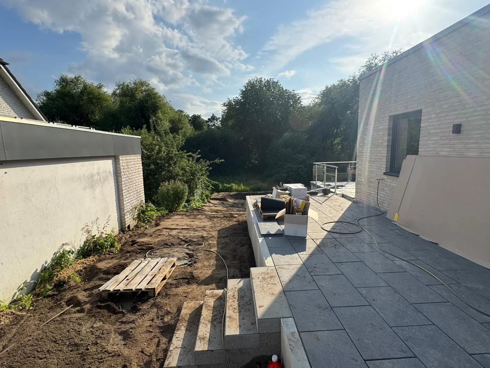 Neu angelegte Terrasse aus großformatigen Betonplatten mit Blockstufen und Stützmauer an einem Neubau im Abendlicht.