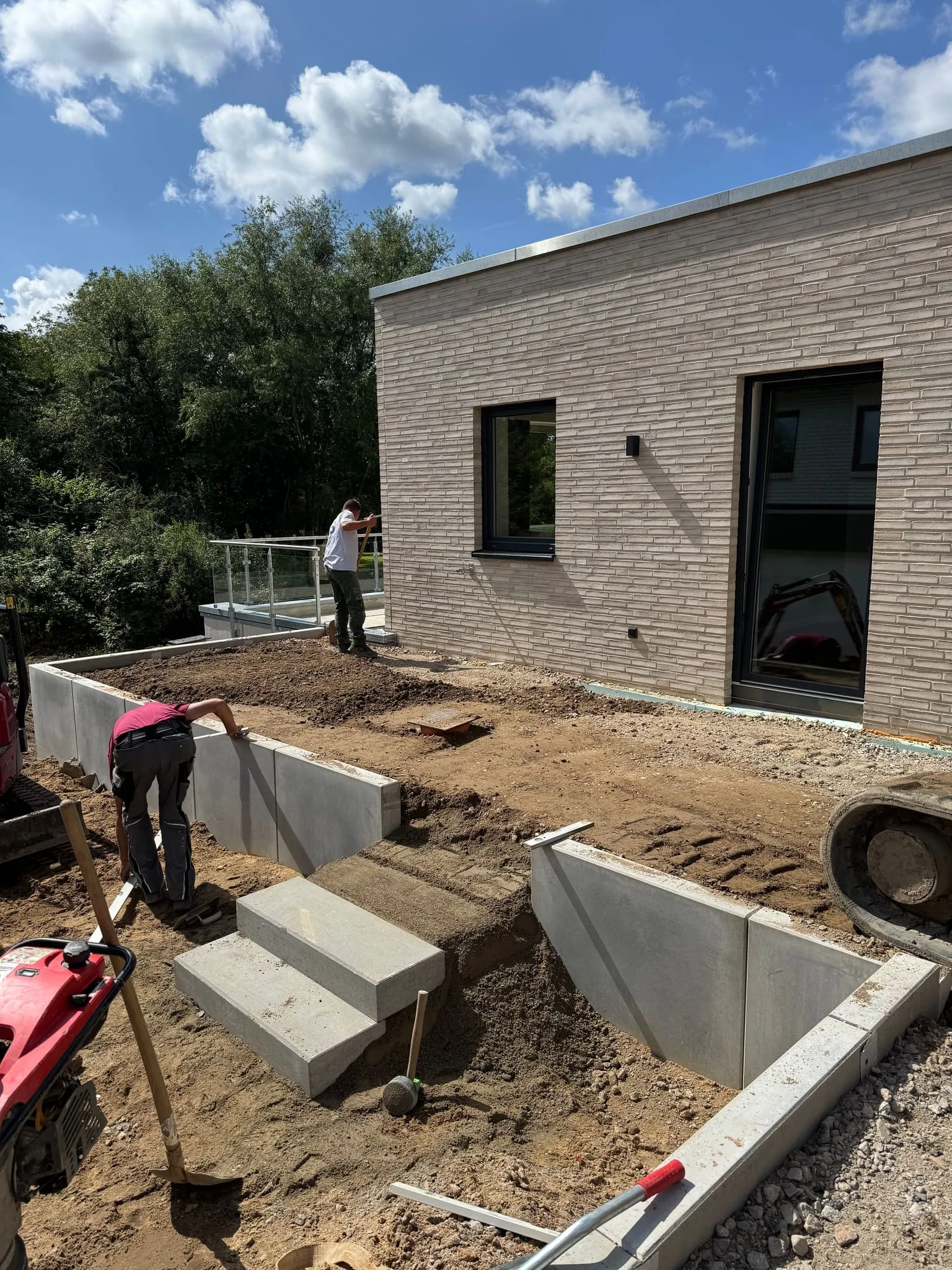 Winkelstützen und Blockstufen am Hang vor einem Neubau, ein Mitarbeiter arbeitet am Unterbau.