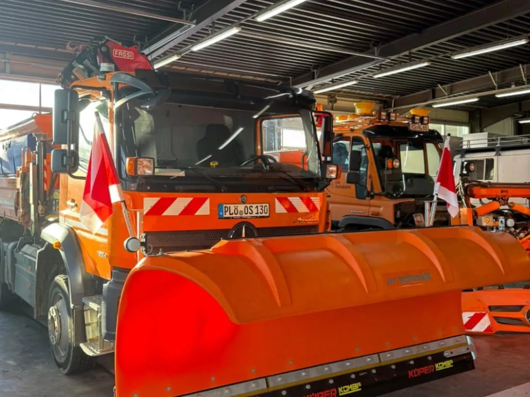 Zwei Winterdienstfahrzeuge mit montierten orangen Schneepflügen stehen einsatzbereit in der Fahrzeughalle