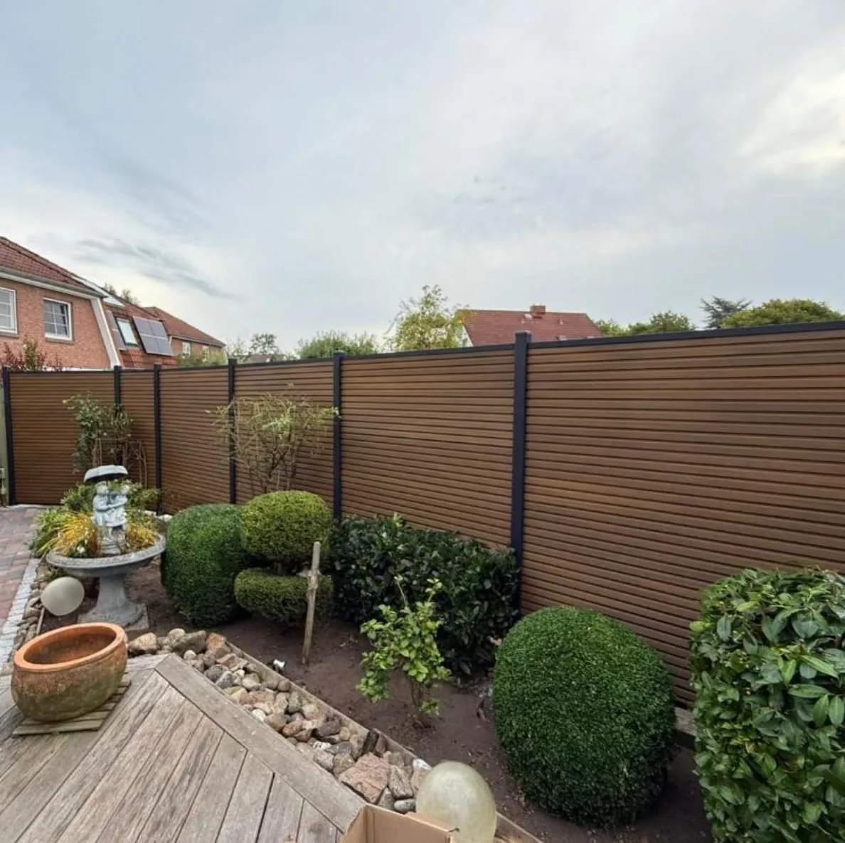 Neu errichteter Sichtschutzzaun in Holzoptik mit anthrazitfarbenen Pfosten rund um eine Terrasse mit Buchskugeln und Steinbeet.
